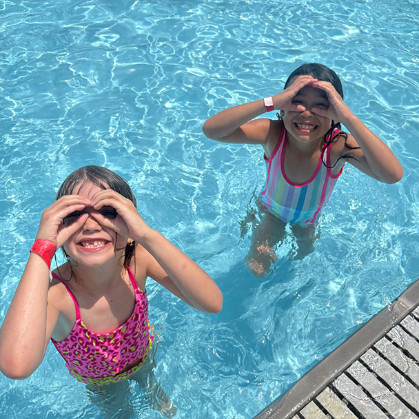 Photo of two smiling girls playing in the pool, holding hands over eyes as imaginative binoculars.